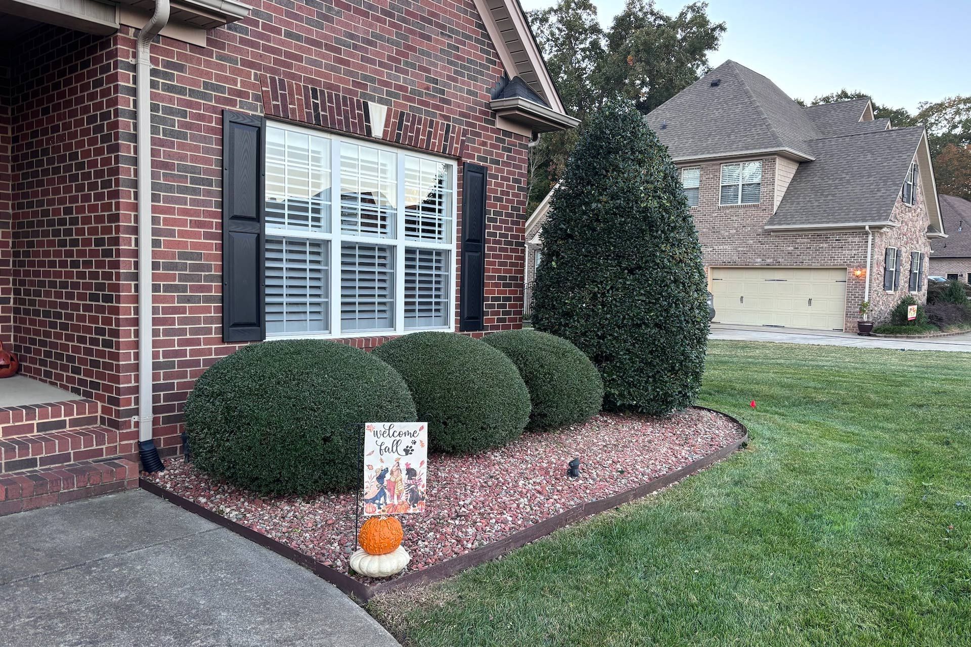 Brick house with dark shutters, shrubbery in a landscaped bed, and a Halloween decoration.