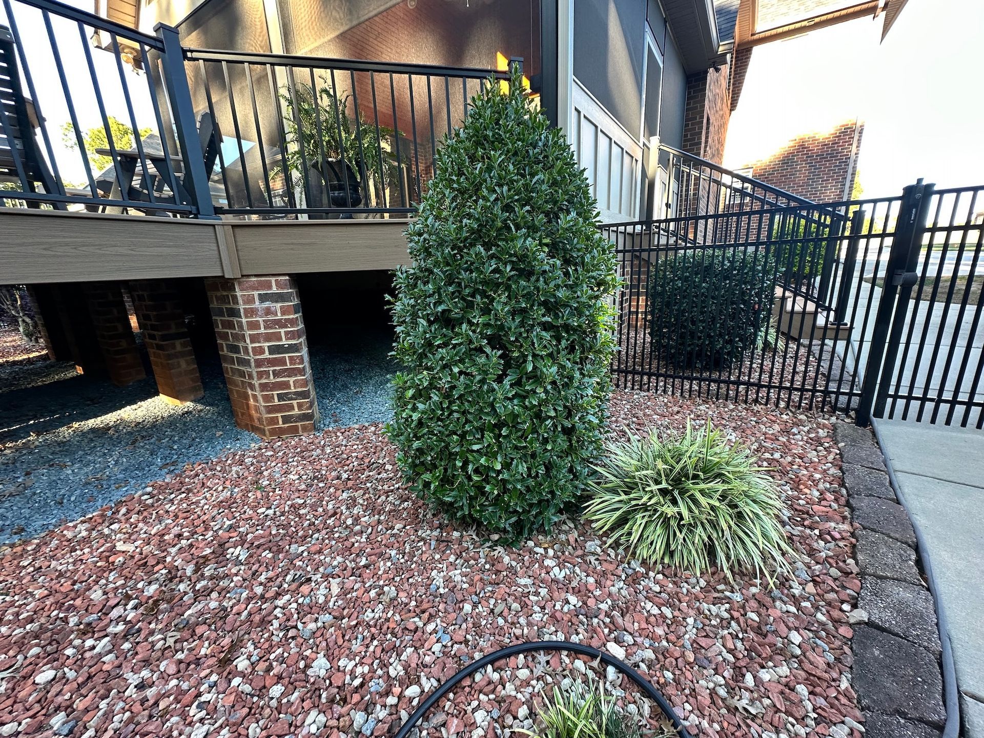Red-rock landscaped yard with evergreen shrubs, deck, black fence, and brick supports.