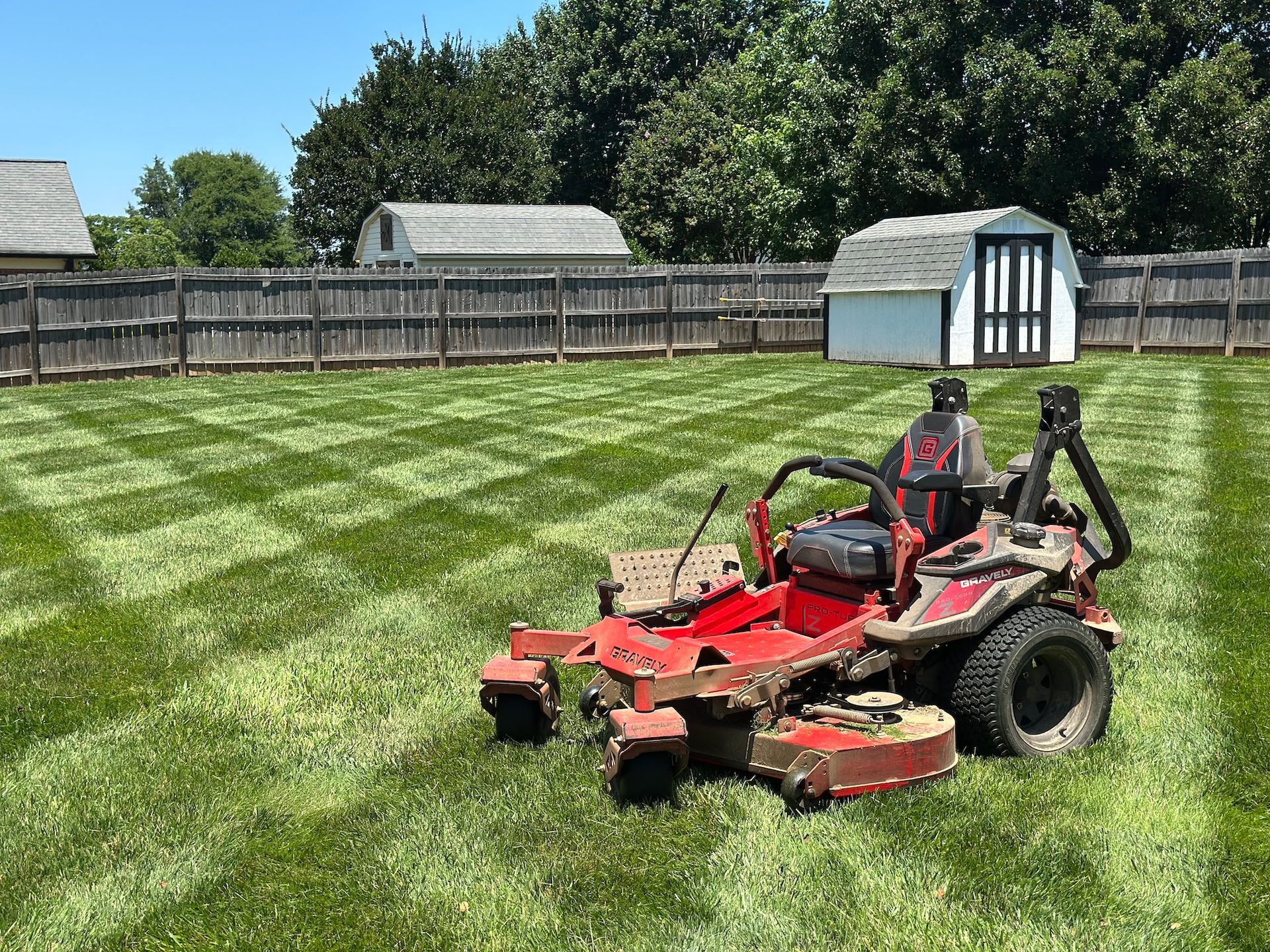 Red zero-turn lawnmower on a neatly mowed lawn in a backyard with a fence and shed.