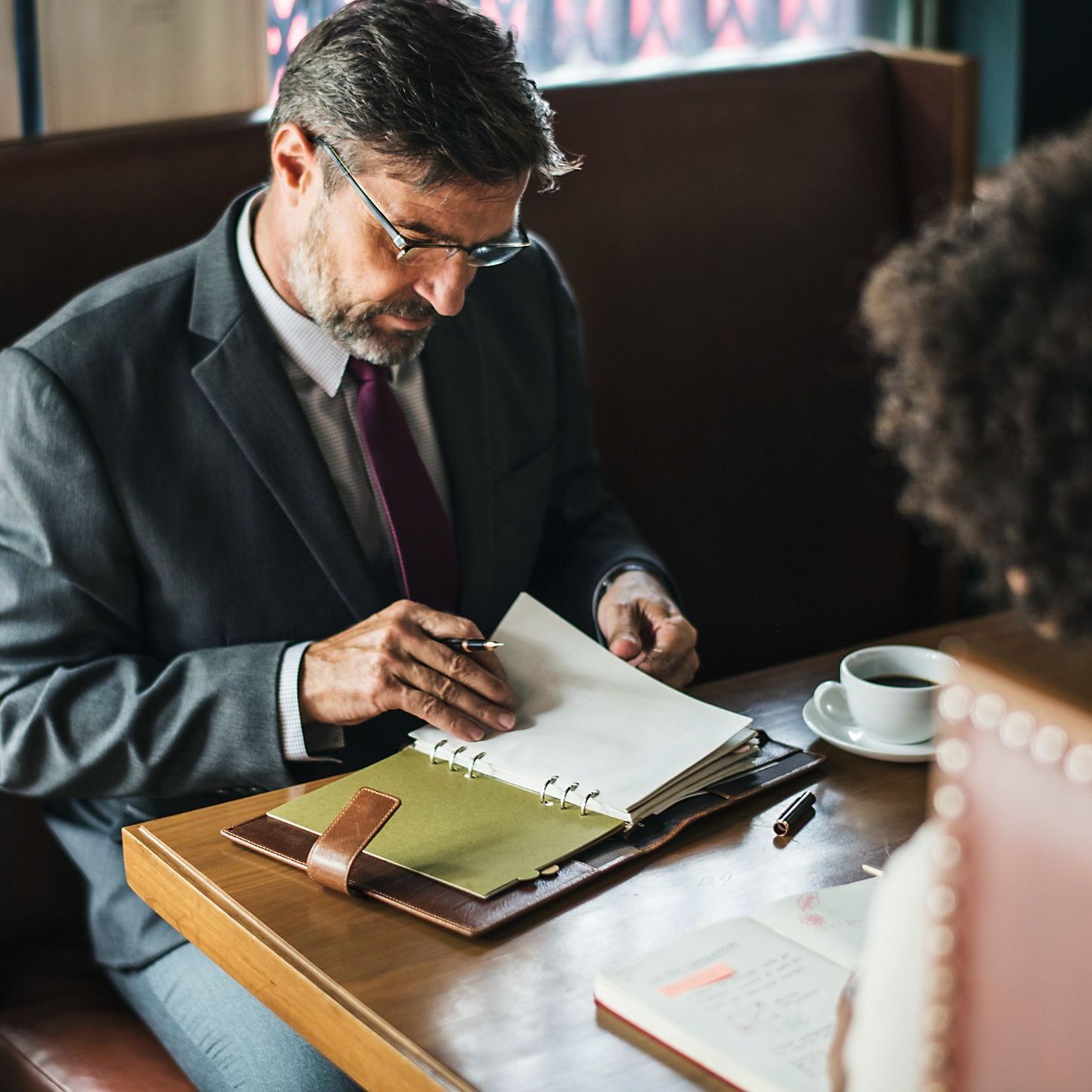 A man in a suit and tie is sitting at a table looking at a notebook.