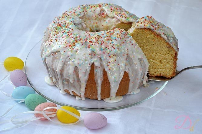 Una ciambella con glassa e granelli di zucchero su un piatto di vetro con uova di Pasqua sullo sfondo.