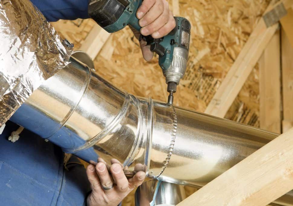 A man is working on a metal pipe with a drill.