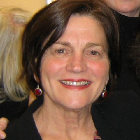 A woman wearing a black jacket and red earrings smiles for the camera