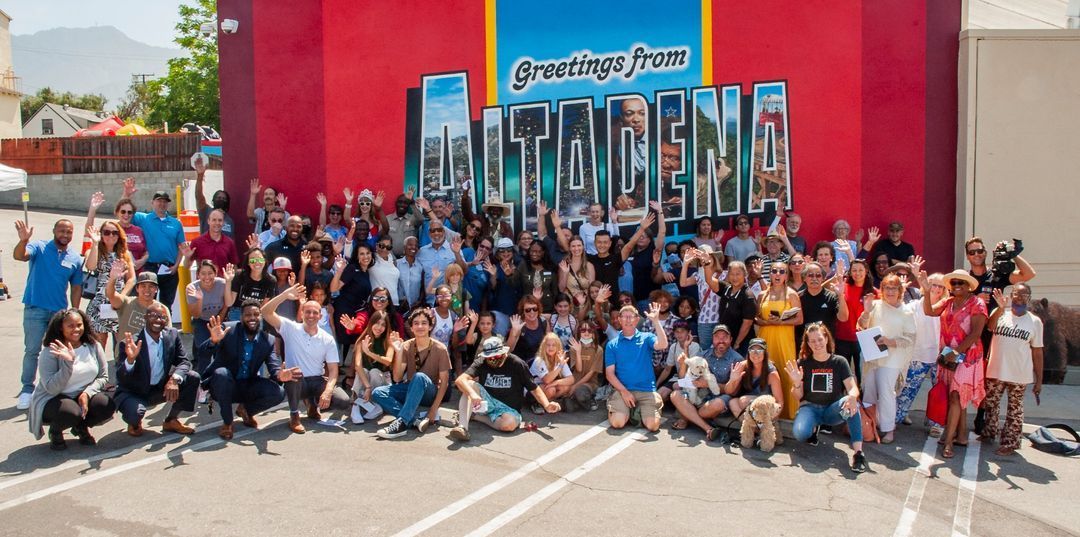 A large group of people are posing for a picture in front of a mural that says greetings from Altadena.