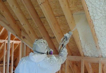 A man is spraying foam on the ceiling of a house under construction.