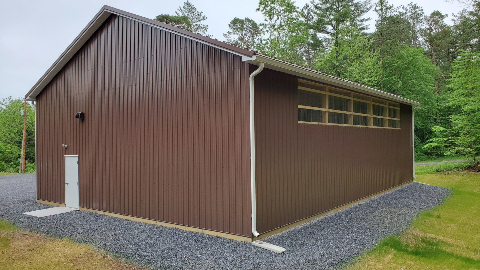 A brown metal building with a white door is sitting in the middle of a field.