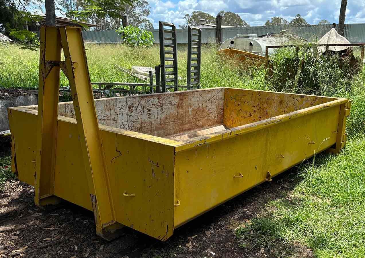A yellow dumpster is sitting in the grass in a field.
