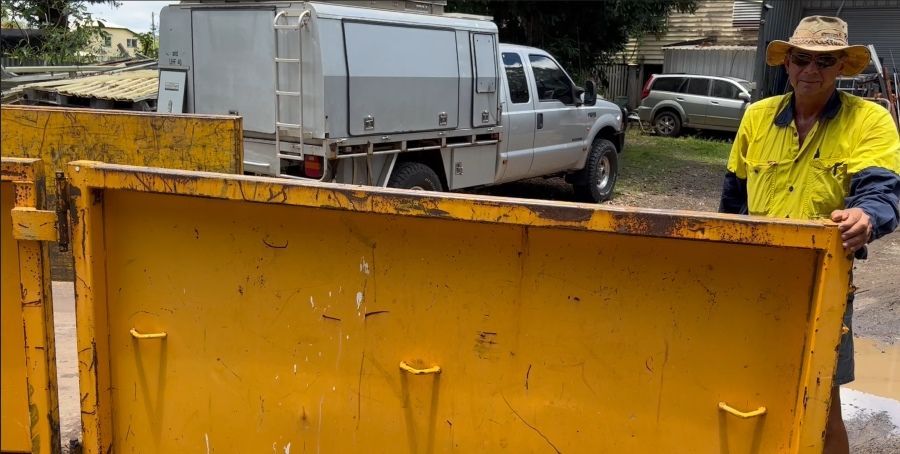 A Man in a Cowboy Hat is Standing Next to a Yellow Dumpster — Bin Hire in Maryborough, QLD