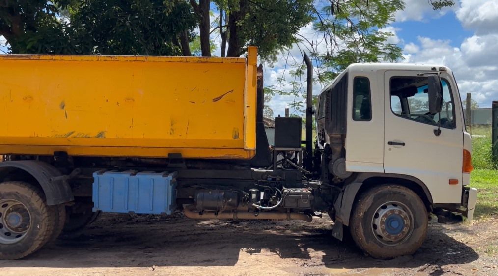 A Yellow Dump Truck is Parked in a Dirt Lot Next to a Tree — Bin Hire in Hervey Bay, QLD