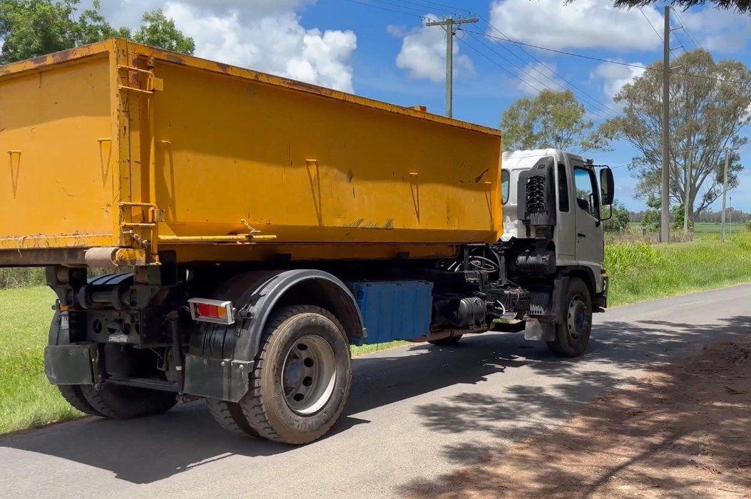 A Yellow Dump Truck is Parked on the Side of a Road — Bin Hire in Hervey Bay, QLD