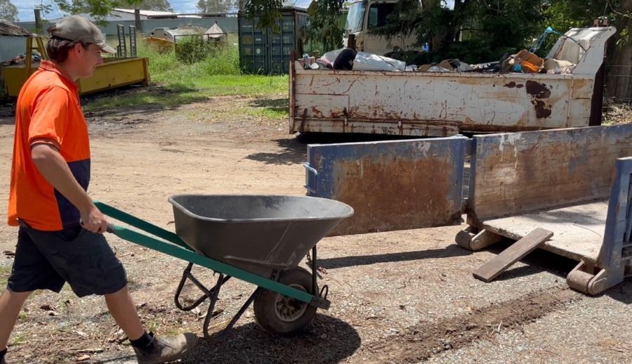 A Man is Pushing a Wheelbarrow in a Dirt Field — Bin Hire in Hervey Bay, QLD