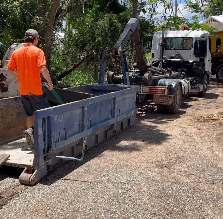 A Man in an Orange Shirt is Standing Next to a Dumpster — Bin Hire in Maryborough, QLD