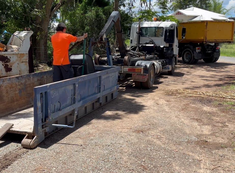 A Man in an Orange Shirt is Loading a Dumpster Into a Truck — Bin Hire in Maryborough, QLD