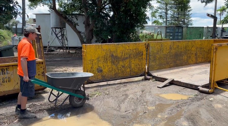 A Man is Pushing a Wheelbarrow in a Muddy Area — Bin Hire in Maryborough, QLD
