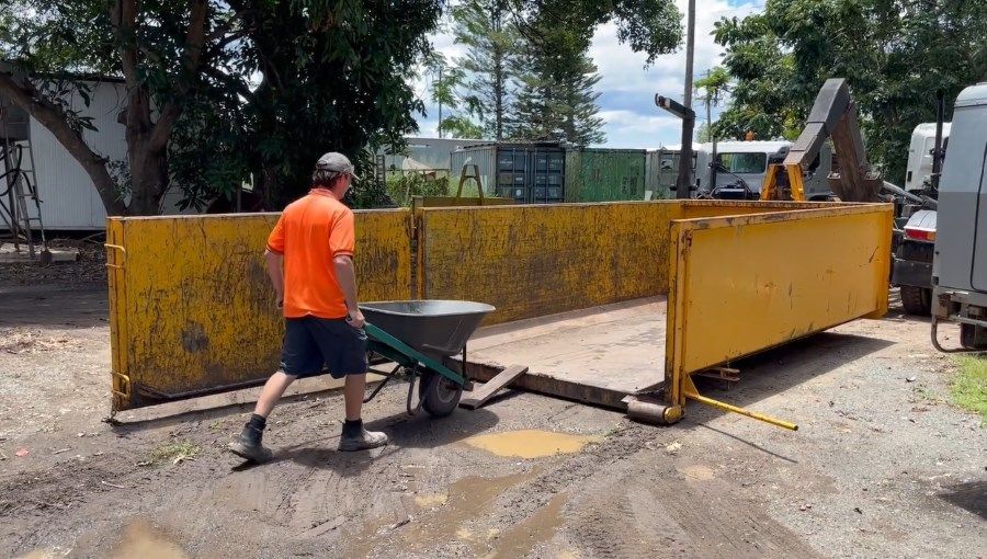 A Man is Pushing a Wheelbarrow Into a Dumpster — Bin Hire in Maryborough, QLD