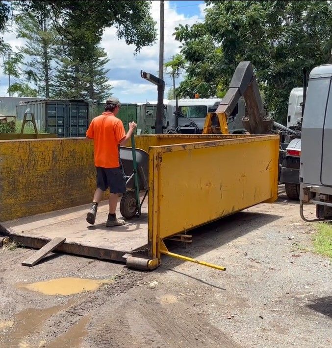 A Man Pushing a Wheelbarrow Next to a Yellow Dumpster — Bin Hire in Maryborough, QLD