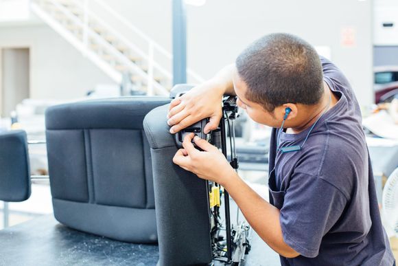 A man is working on a car seat in a factory.