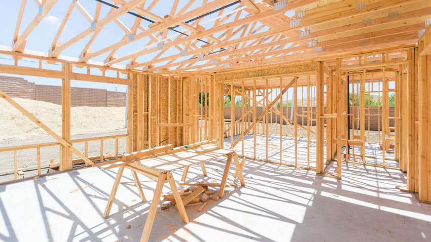 Wood-framed house under construction with exposed roof trusses and bright sunlight