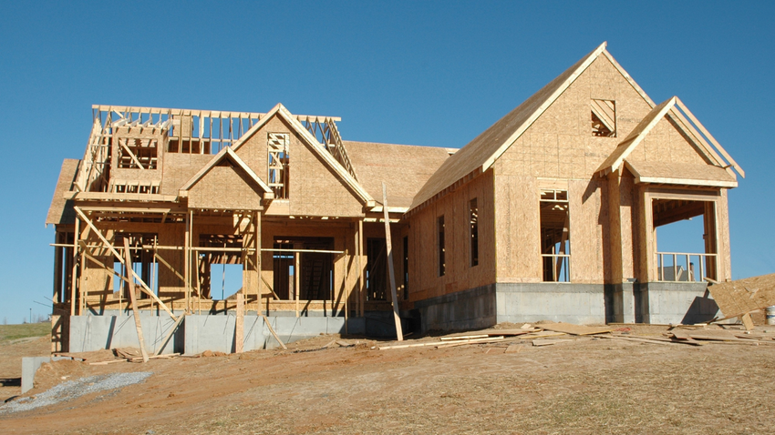 Two unfinished wooden houses under construction on a dirt lot, with exposed framing and roof trusses.