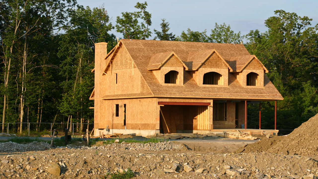 Partially built wooden house on a cleared lot with trees in the background
