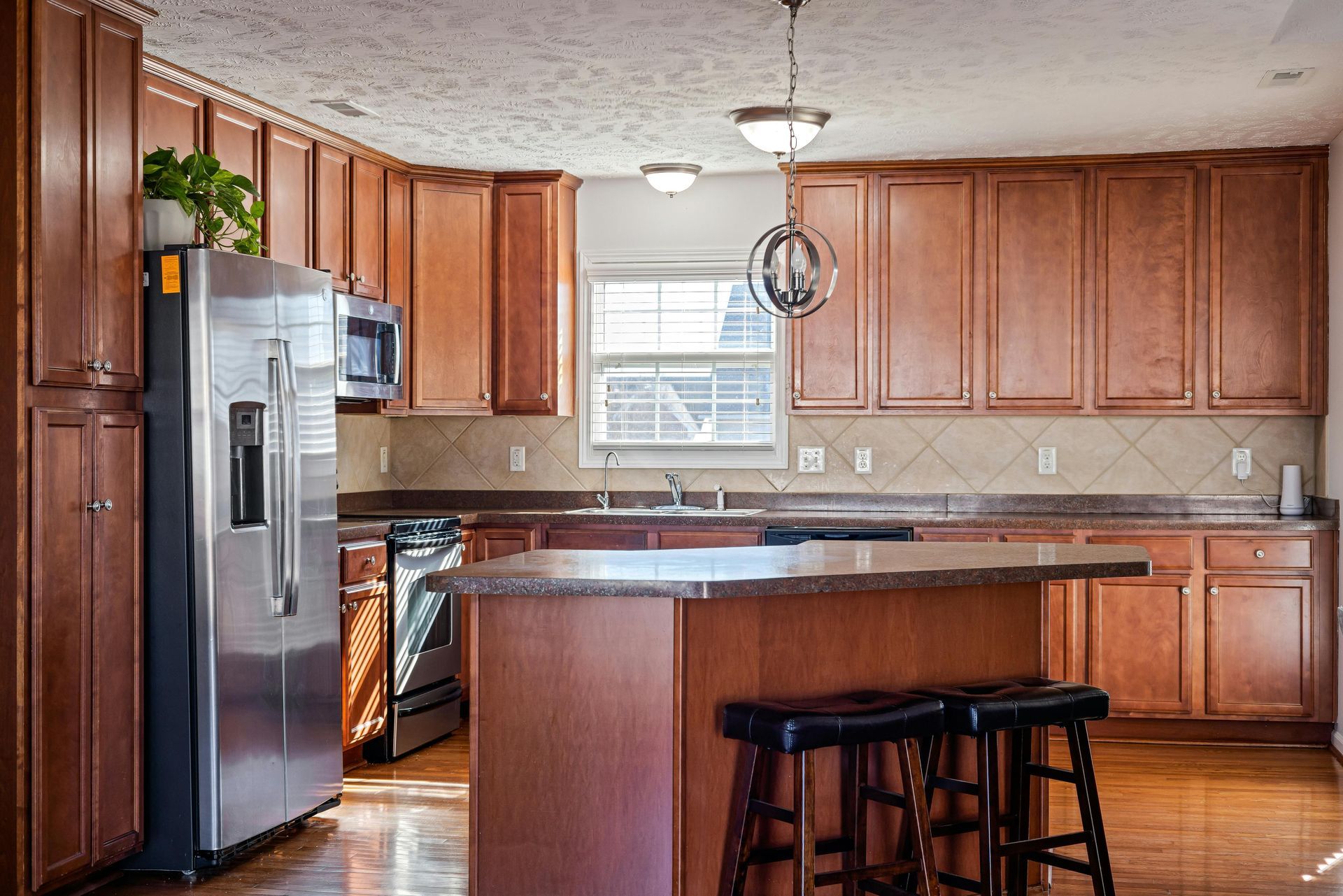 Kitchen with wooden cabinets, stainless steel appliances, dark countertops, and a central island with stools.