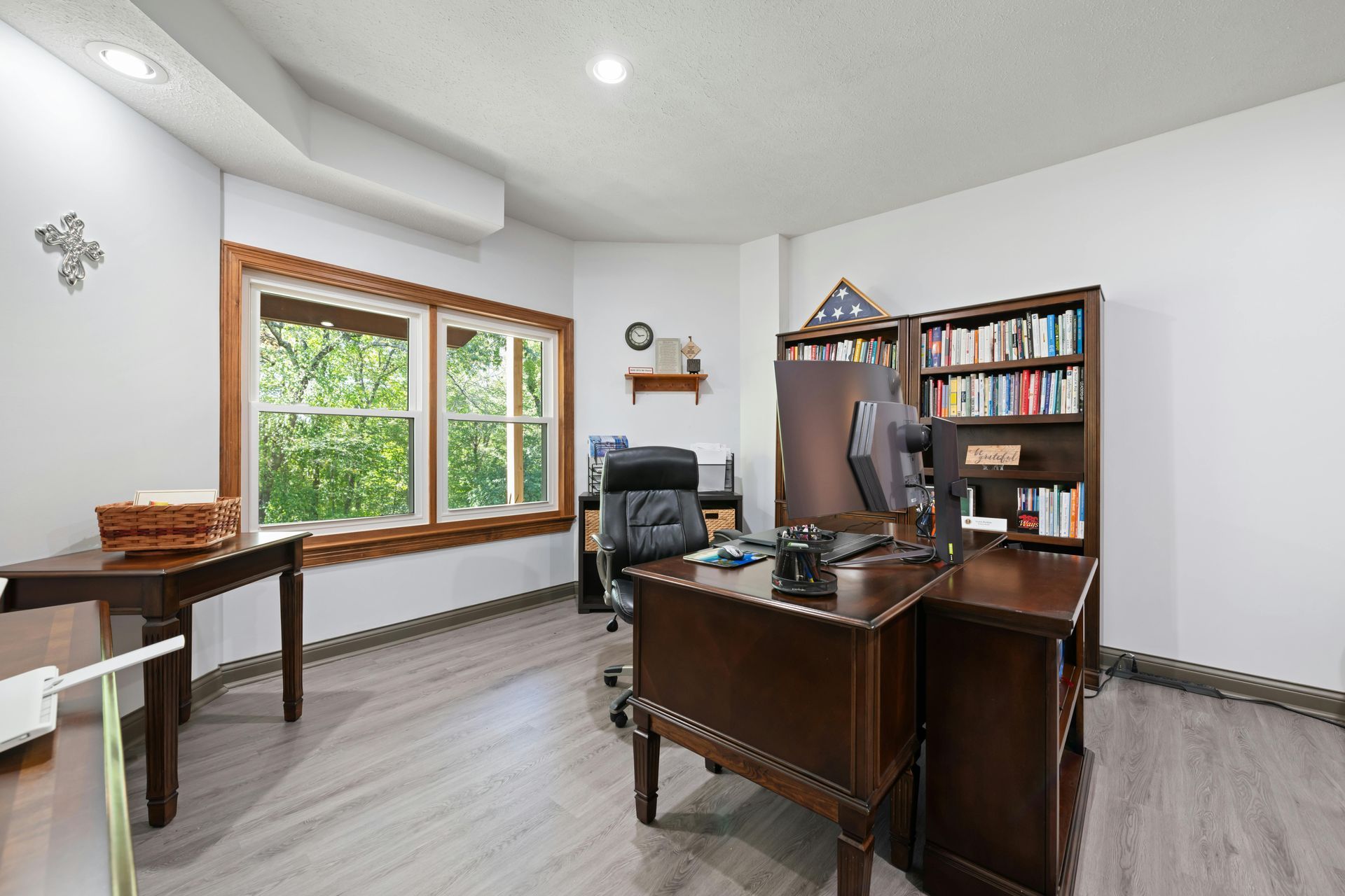Home office with wooden desk, bookcase, chair, and large window overlooking greenery.