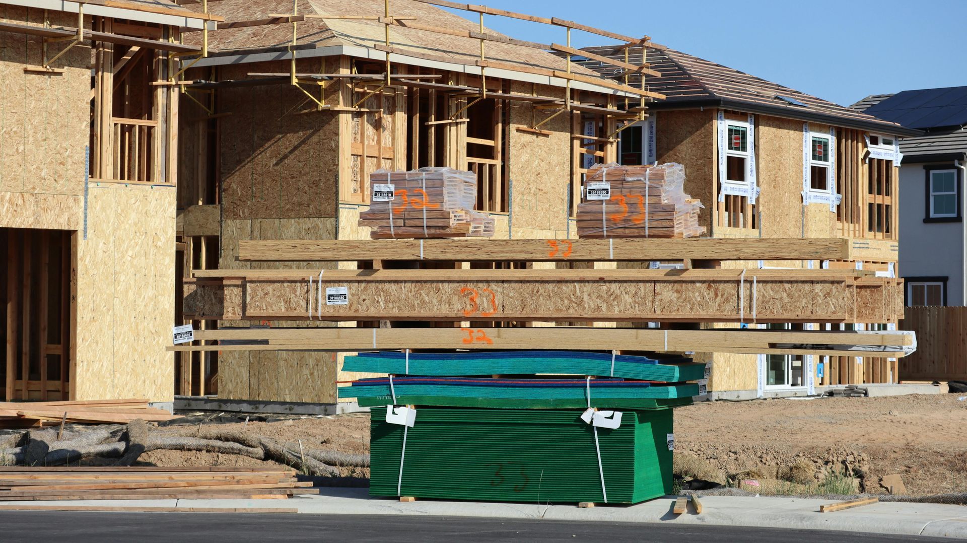 Partially built house under construction with wooden framing, scaffolding, and a green dumpster in front