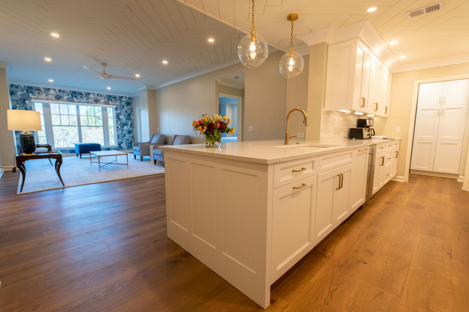Bright open kitchen with white island cabinets, hardwood floors, and a living room visible beyond.