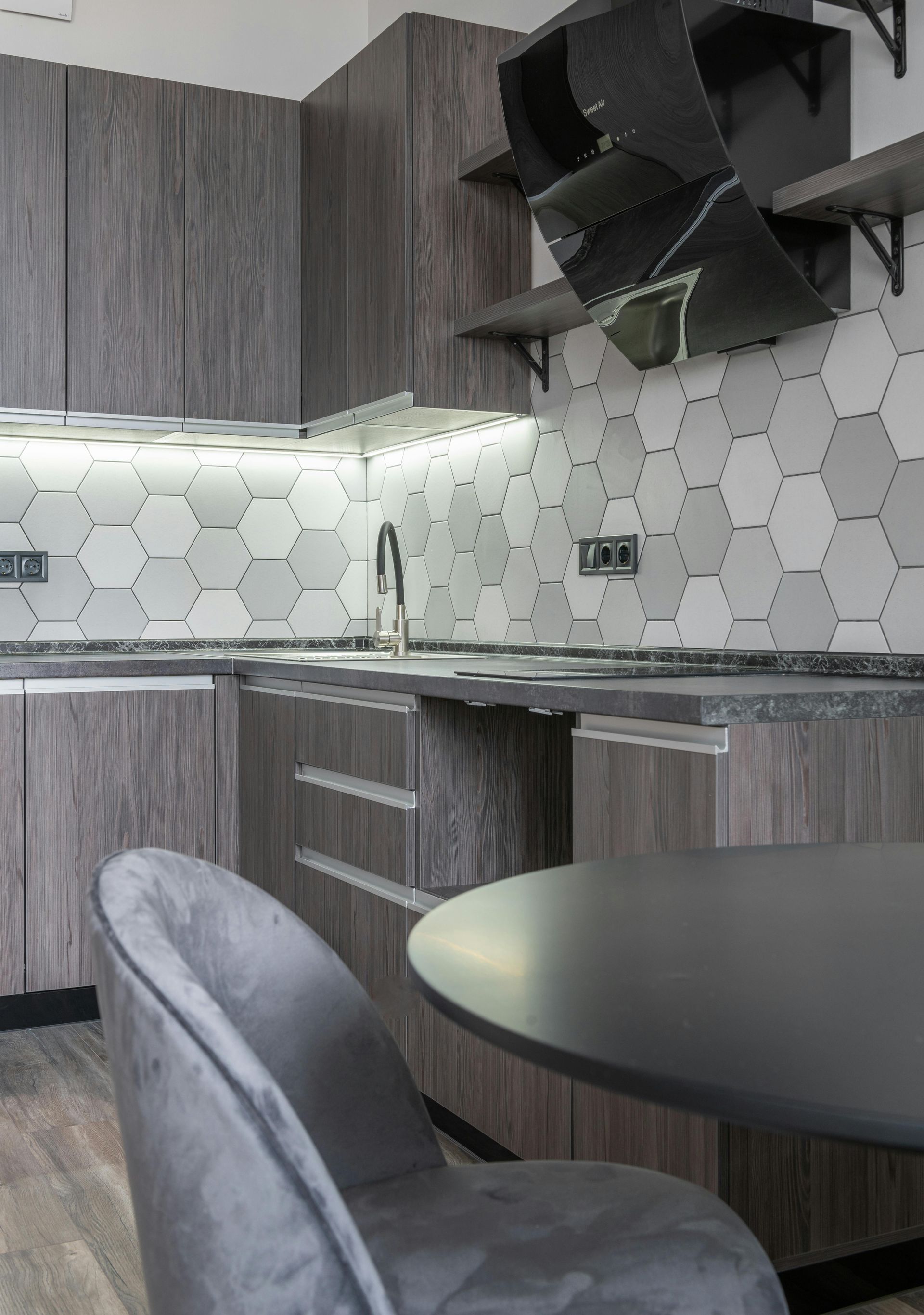 Modern kitchen with gray cabinets, hex tile backsplash, under-cabinet lighting, and a small round table.