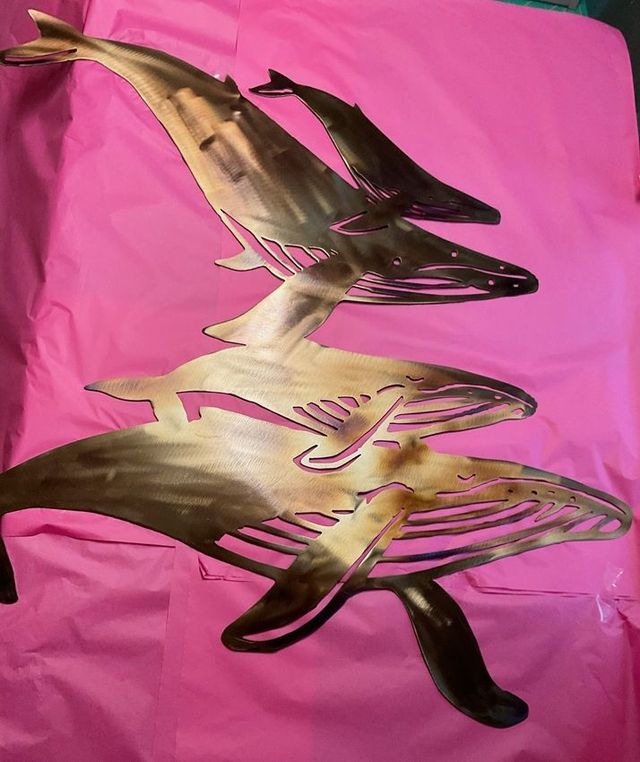 Metal sculpture of whales swimming upwards, set against a pink background.