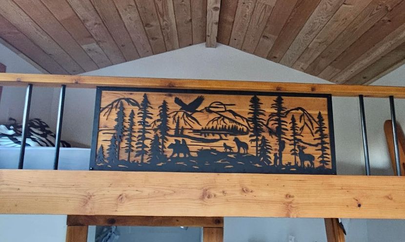 Wooden mountain scene art on a cabin railing, featuring trees, animals, and an eagle silhouette.