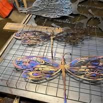 Two metal dragonfly sculptures in blues, purples, and gold, on a metal table.