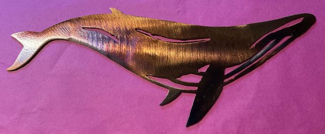 Metal whale sculpture on a pink background.