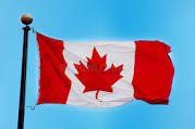 Canadian flag, red and white with a maple leaf in the center, waving in the wind against a blue sky.