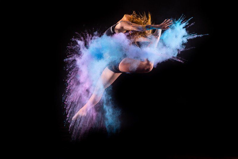 A woman is jumping in the air surrounded by colorful powder.