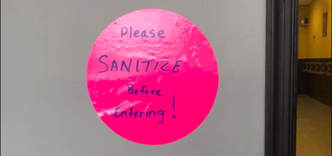 A pink sign on a door that says please sanitize before entering