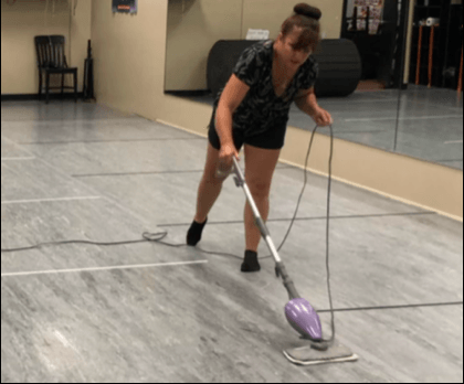 A woman is using a purple mop to clean a dance floor