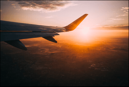 The wing of an airplane is flying in the sky at sunset.