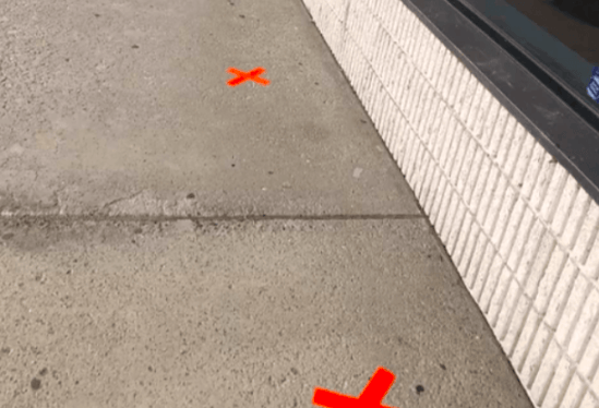 Two orange crosses are painted on the sidewalk in front of a building.