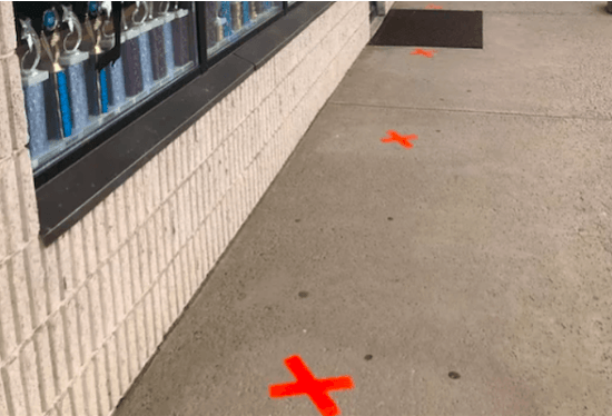 A red cross is painted on the sidewalk in front of a store.