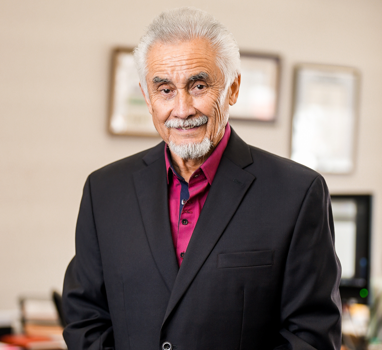 Man in blazer and dress shirt, smiling, standing in an office.