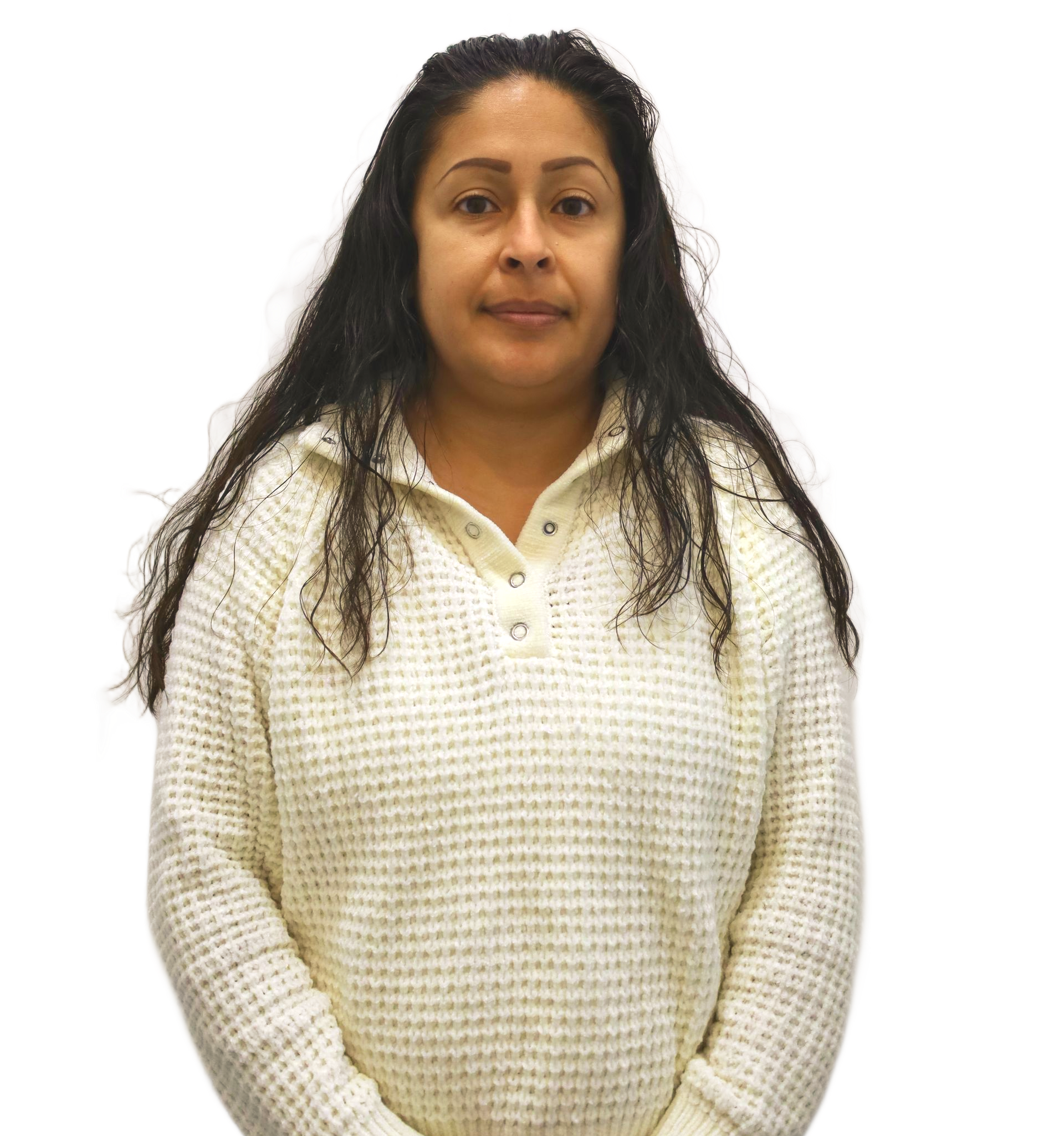 Woman in a white sweater, with long dark curly hair, stands against a white wall.