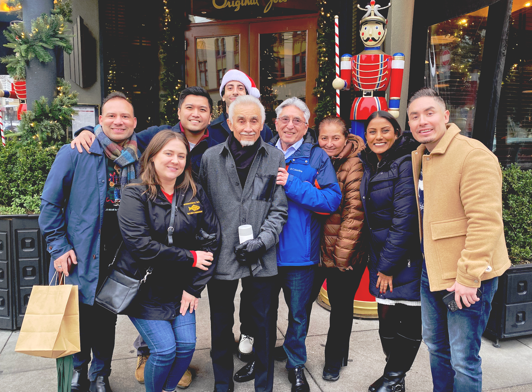 Group of people standing in an office, some with arms around each other. A dog sits in the foreground.