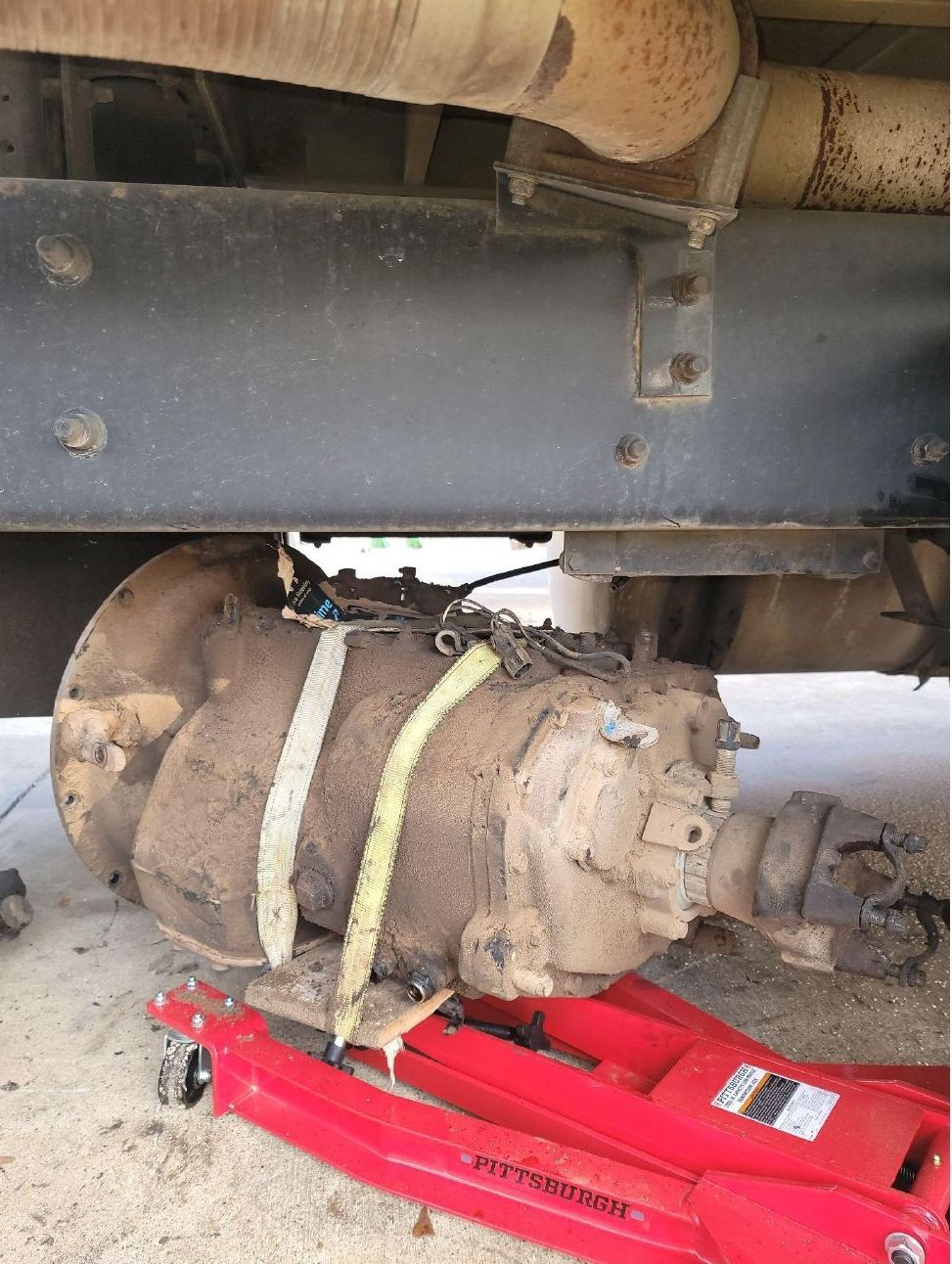 A red jack is sitting under a truck with a gearbox attached to it.