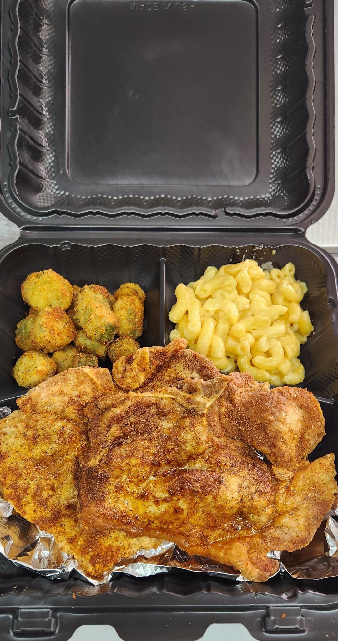 A plastic container filled with fried chicken , macaroni and cheese , and broccoli.