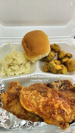 A styrofoam container filled with fried chicken , mashed potatoes , and okra.