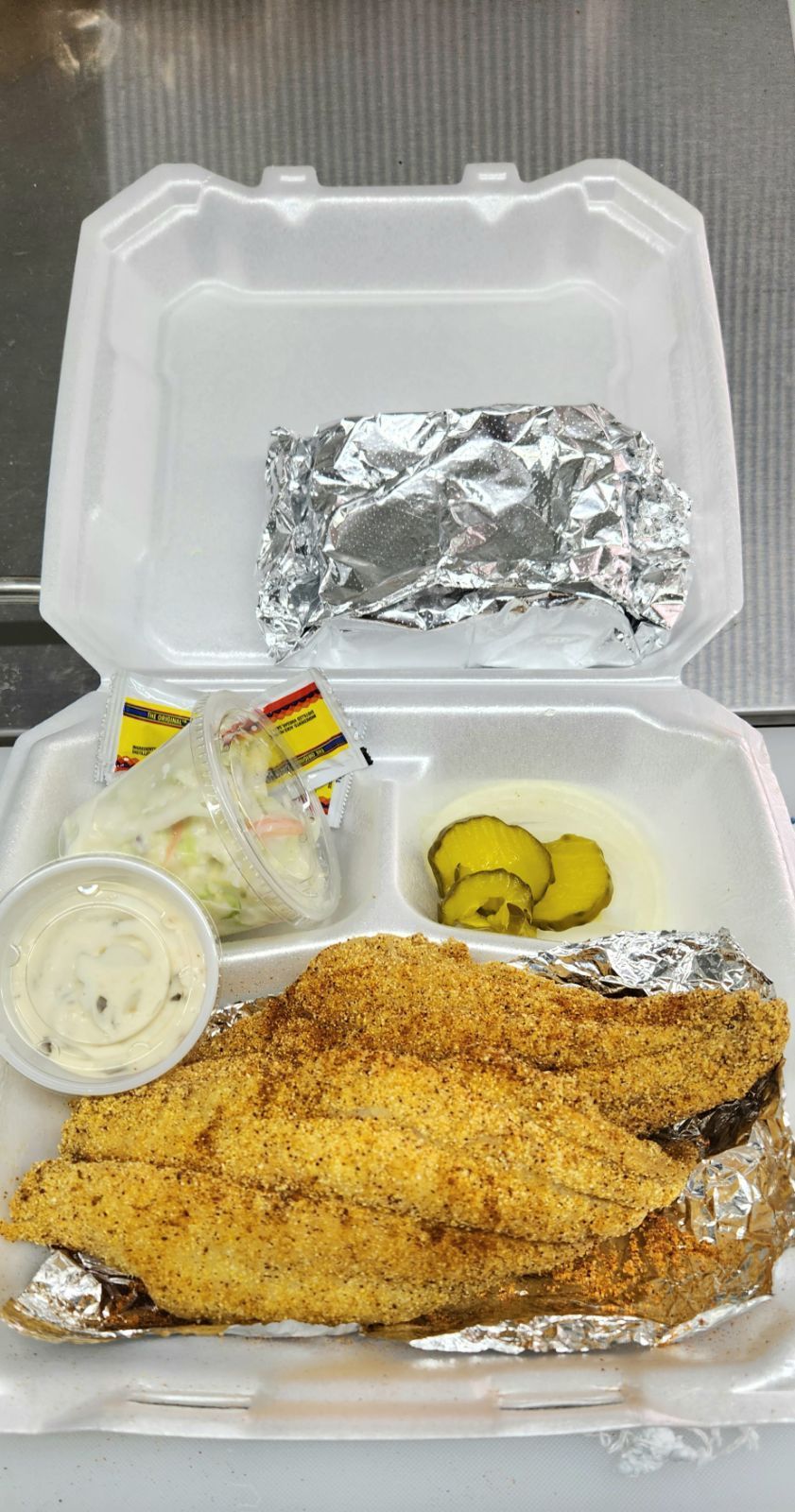 A styrofoam container filled with fried fish , potatoes , and pickles.