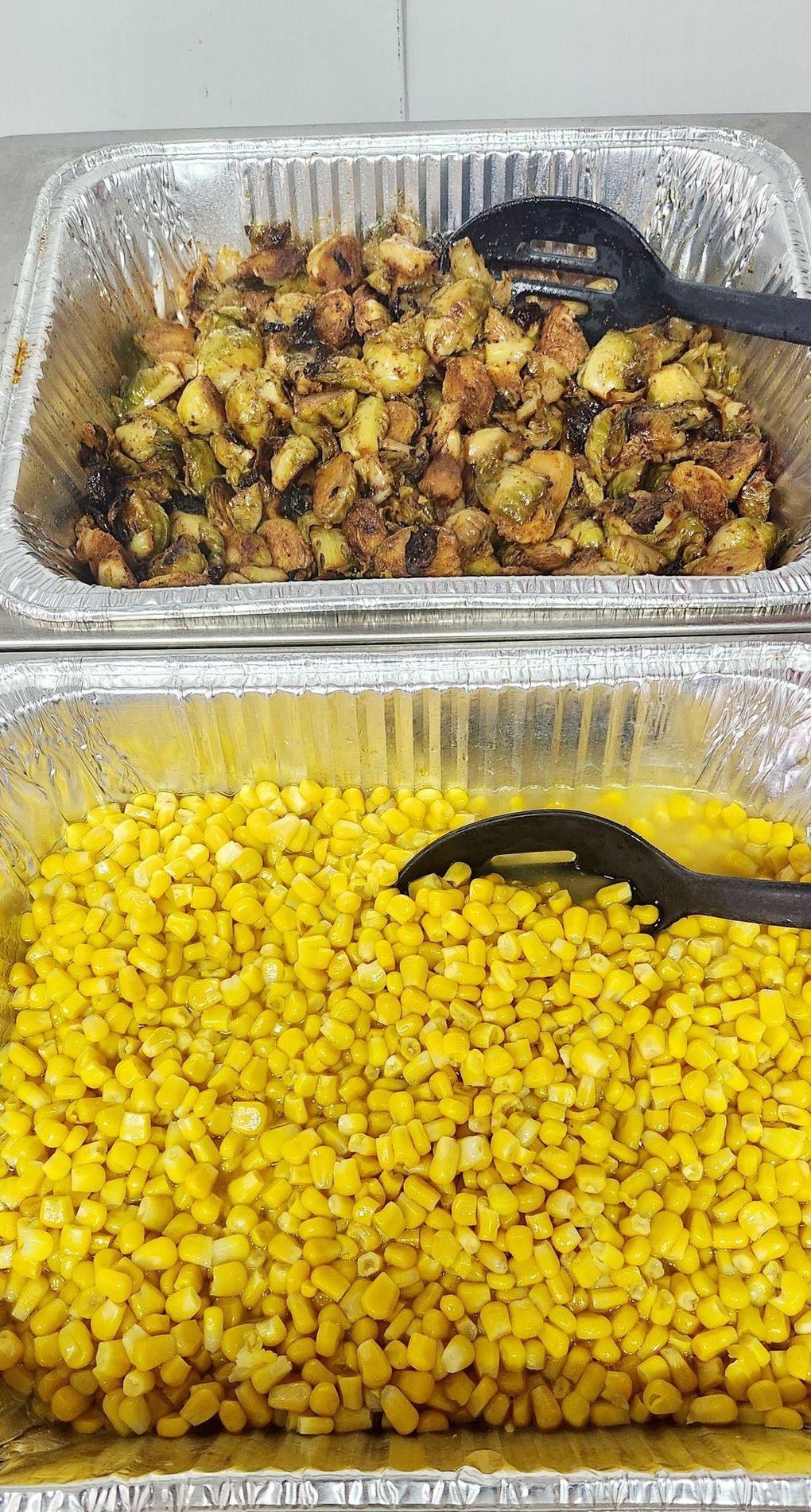 Two trays of food with spoons in them are sitting on a table.