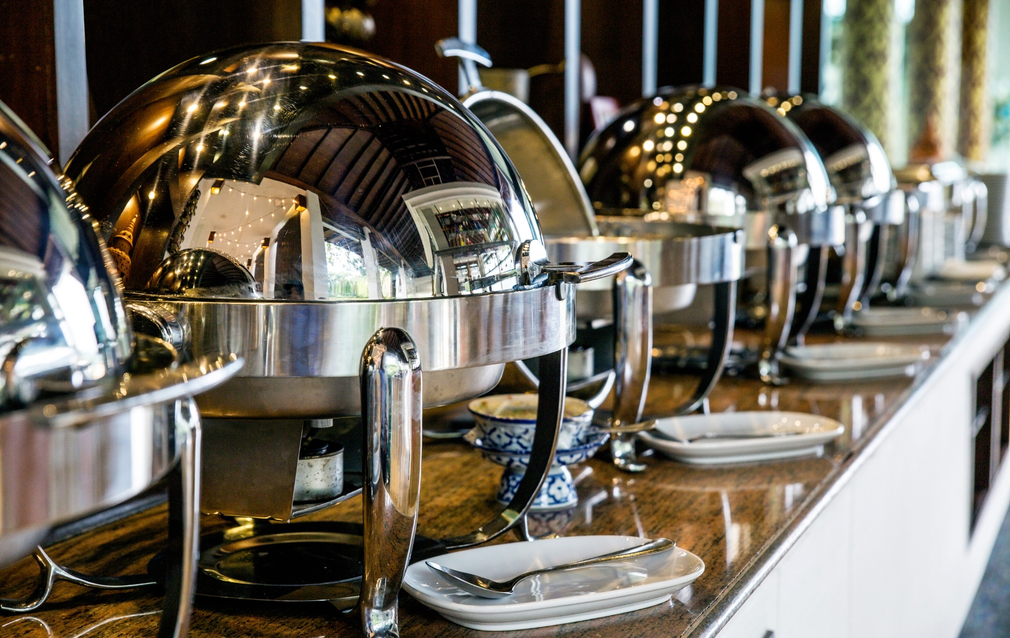 A buffet line with plates and silverware on a counter.