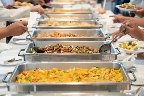 A group of people are eating from buffet trays at a banquet.